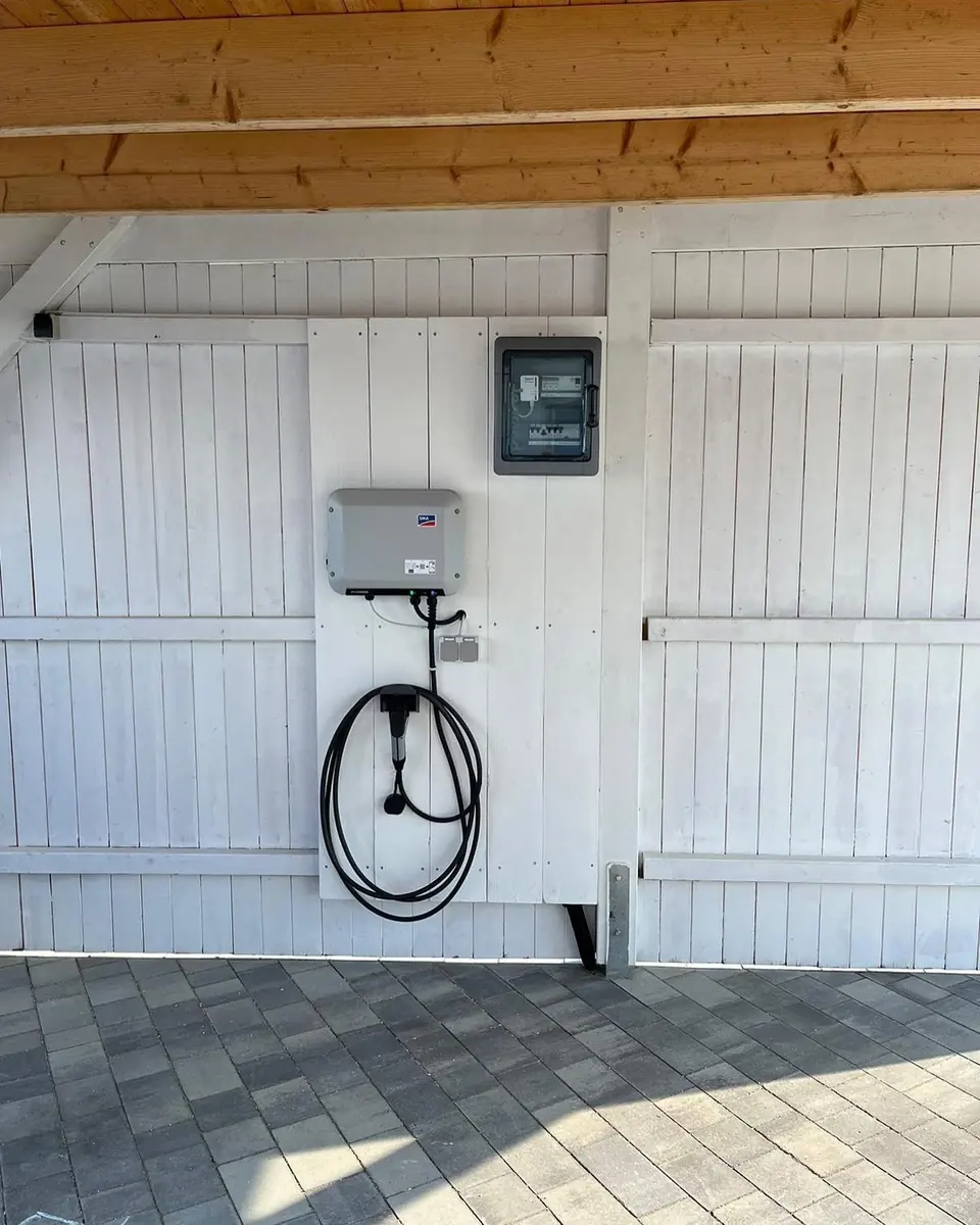 Solarni invertor, mjerni ormarić i kabl za punjenje električnog automobila na zidu nadstrešnice